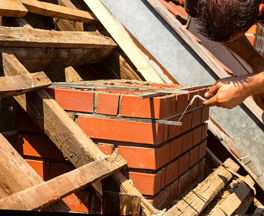 Mason laying new clay brick coursework amid roof timbers